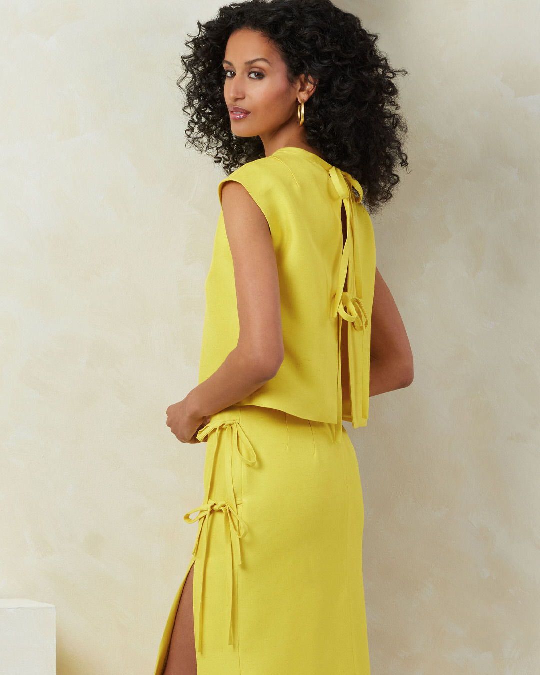 Woman in a yellow dress with curly hair, viewed from the back.