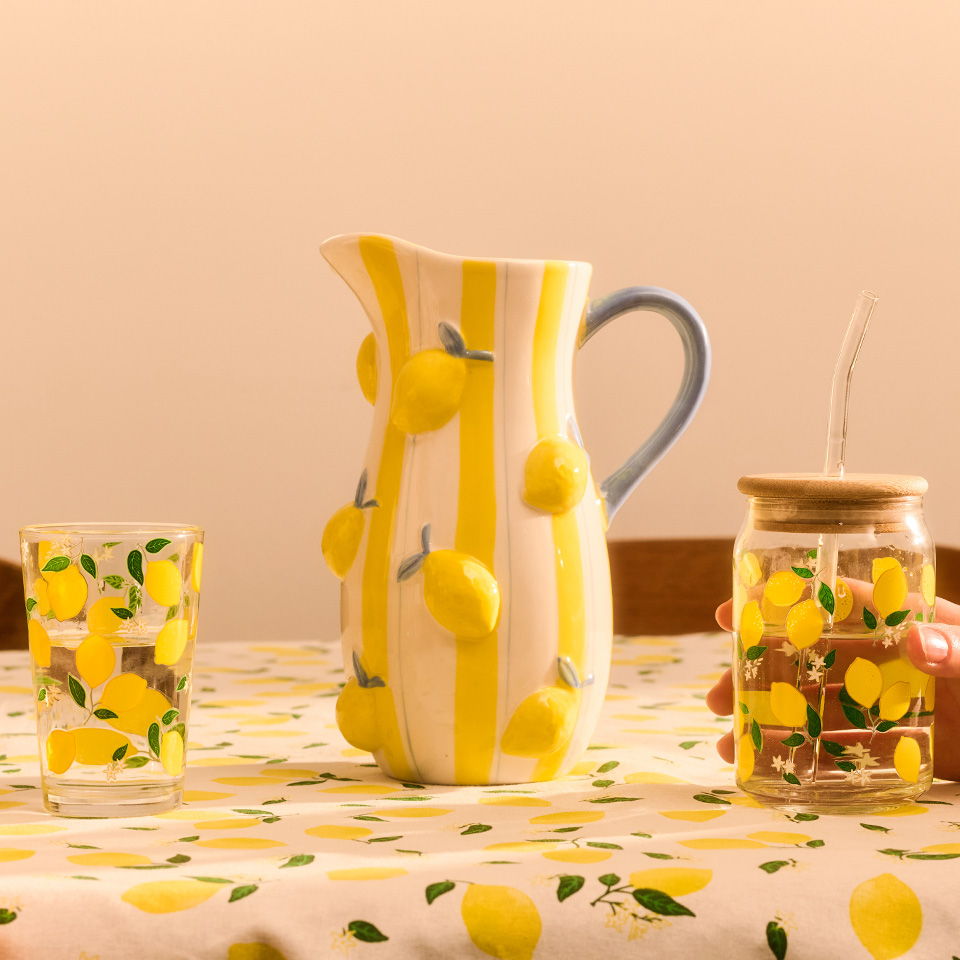 A pitcher and jar with lemon designs on a tablecloth.