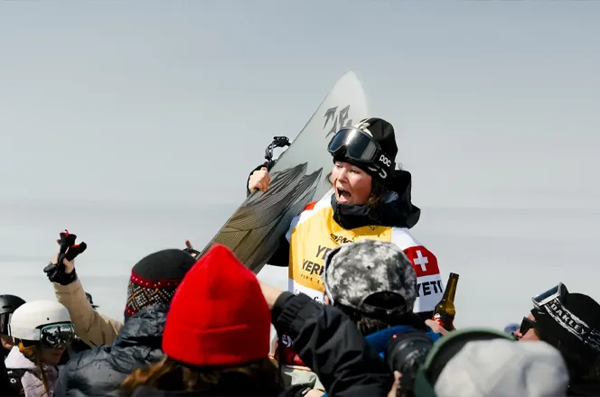Snowboarder Mia Jones celebrating with a trophy surrounded by cheering fans in winter attire.