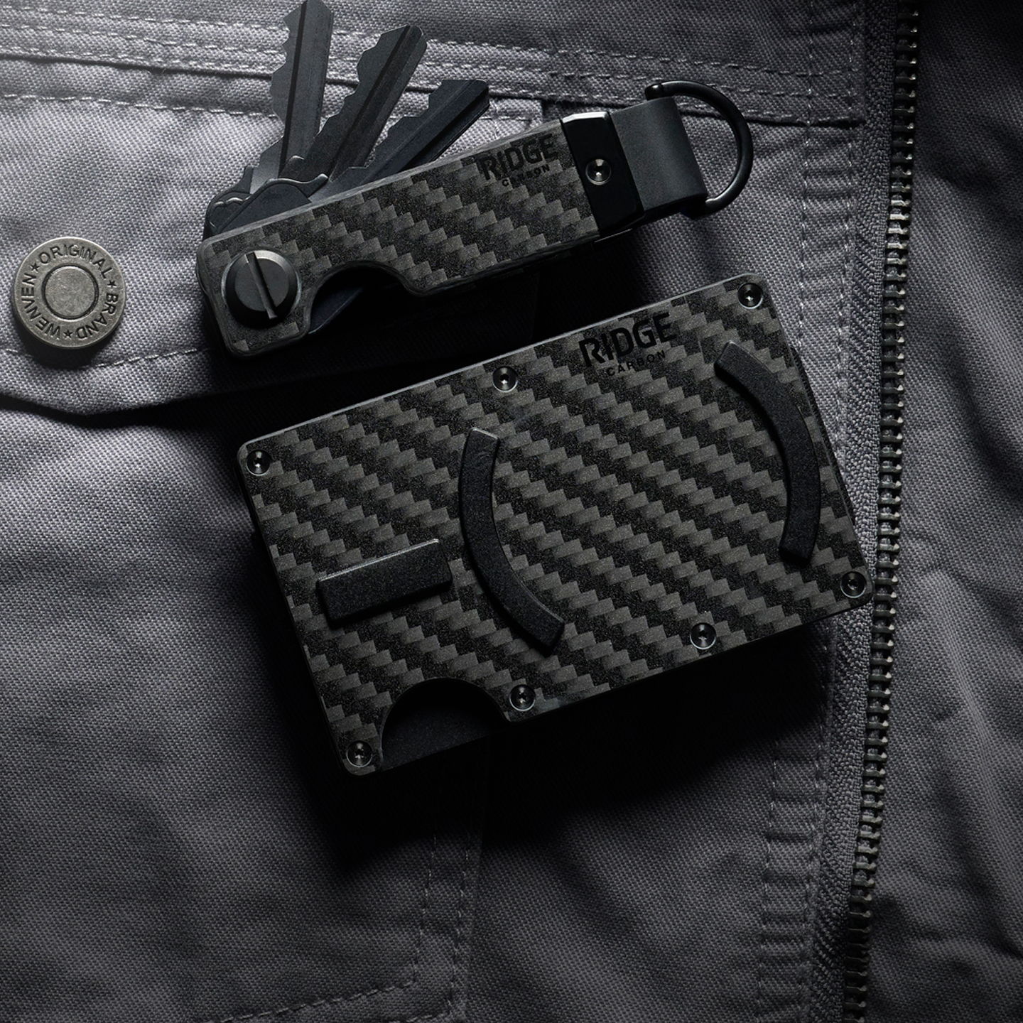 Black carbon fiber wallet and key organizer on a dark fabric background.