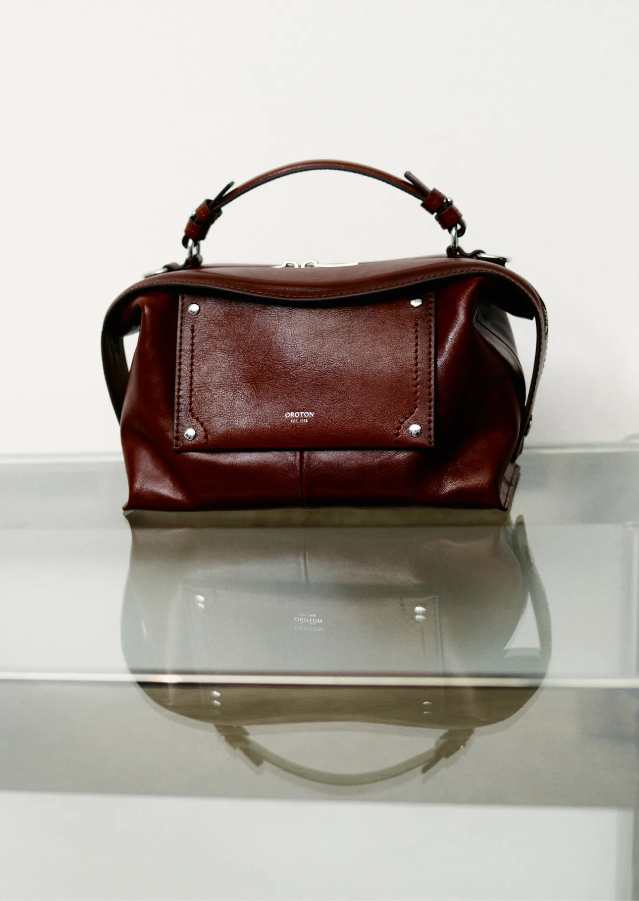 A brown leather handbag on a glass surface.