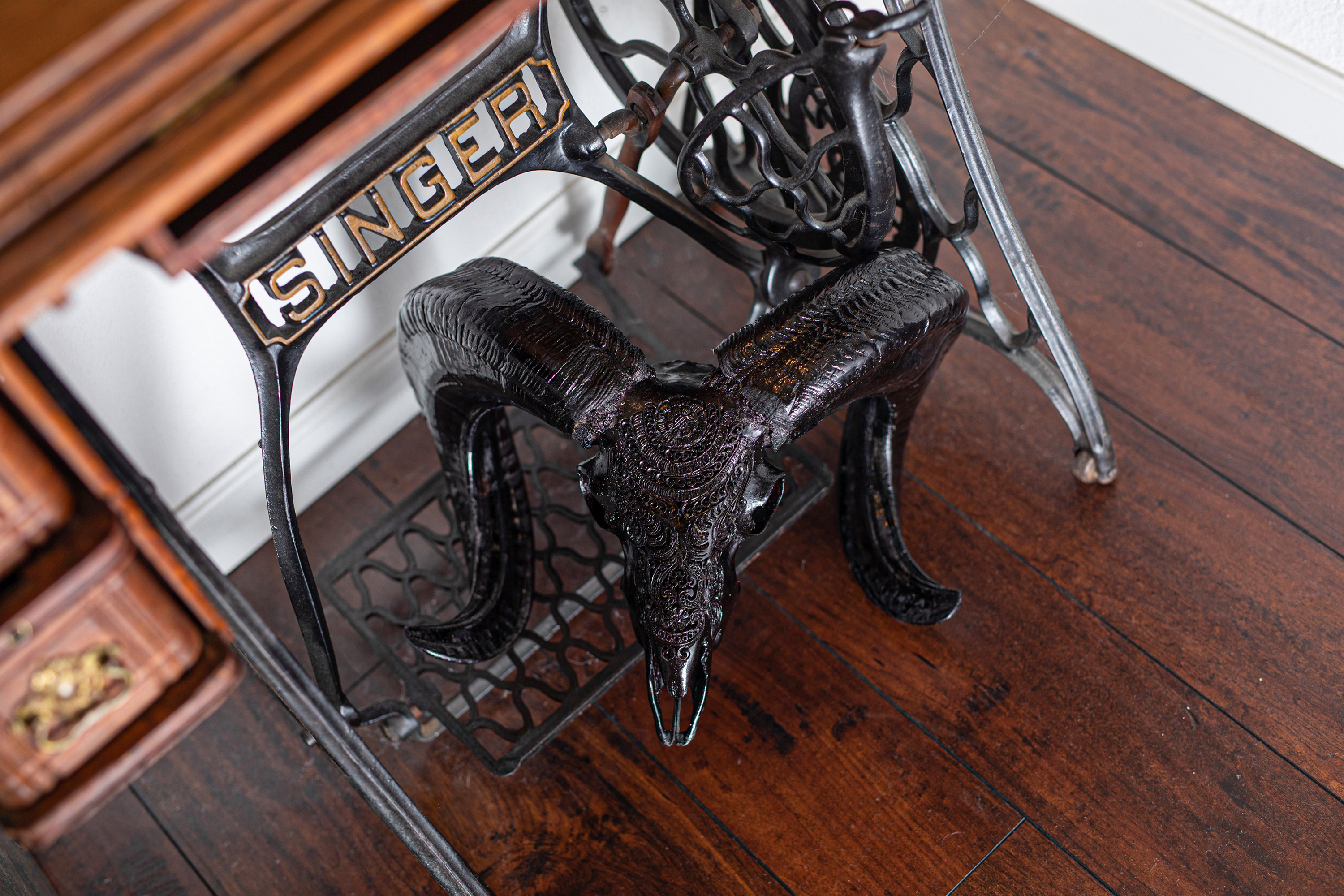 A hand-carved ram skull is laying on a vintage Singer sewing machine. 