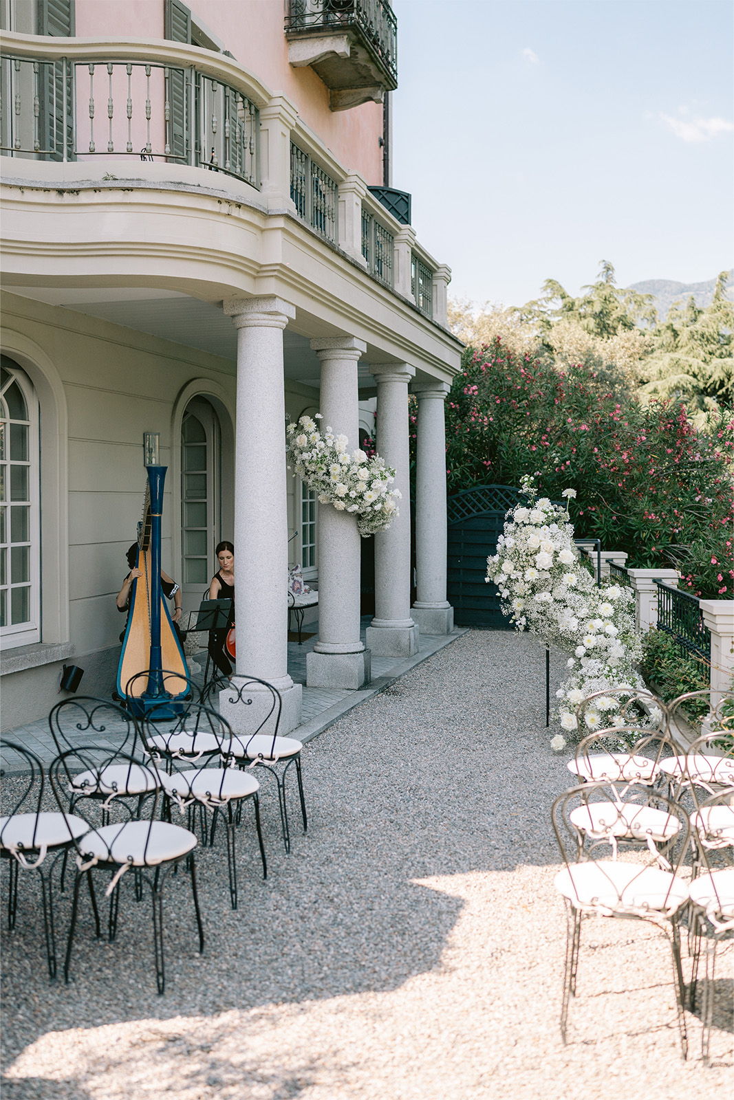 Outdoor event setup with chairs, harpist, and floral decorations near a building.