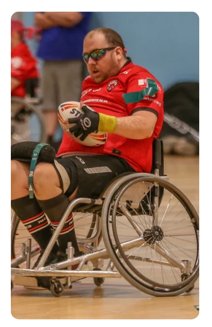 Man in wheelchair rugby uniform holding a rugby ball, focused on play.
