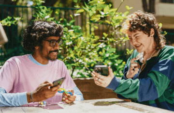 Two friends enjoying time outdoors, looking at their phones.