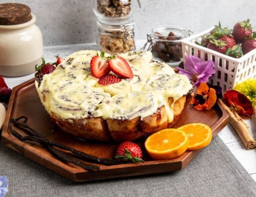 A decorated cake with strawberries and orange slices on a wooden platter.