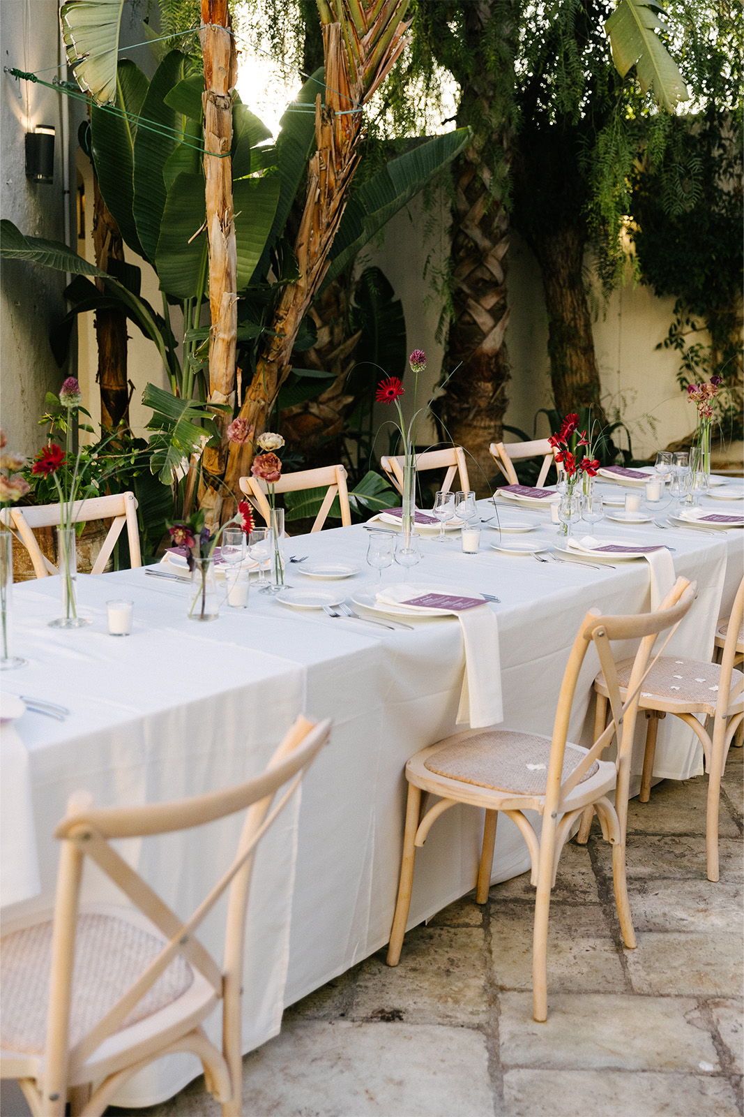 Long dining table set with flowers in a garden.