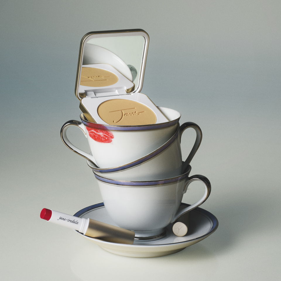 Three stacked teacups with a compact mirror and lipstick.