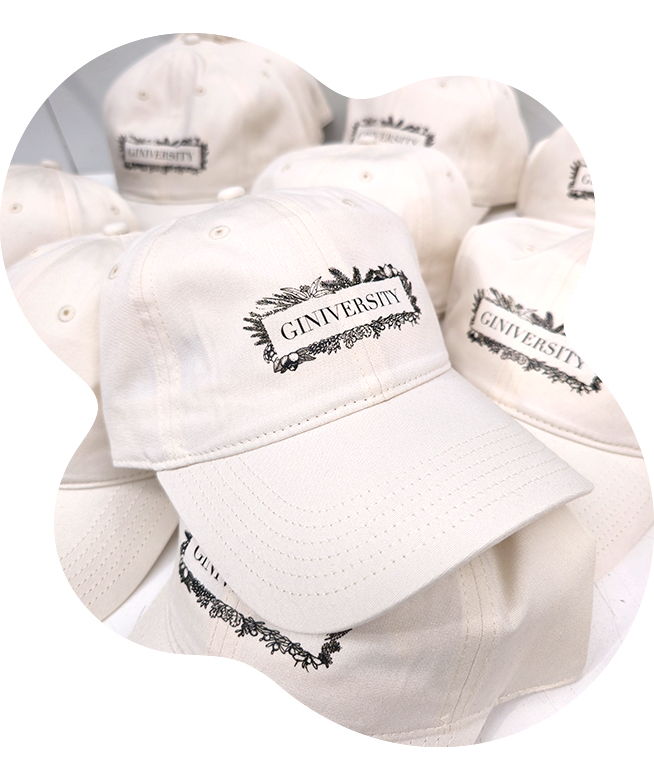 Pile of cream Giniversity caps with a delicate black botanical border and Giniversity DTF printed design on front panel