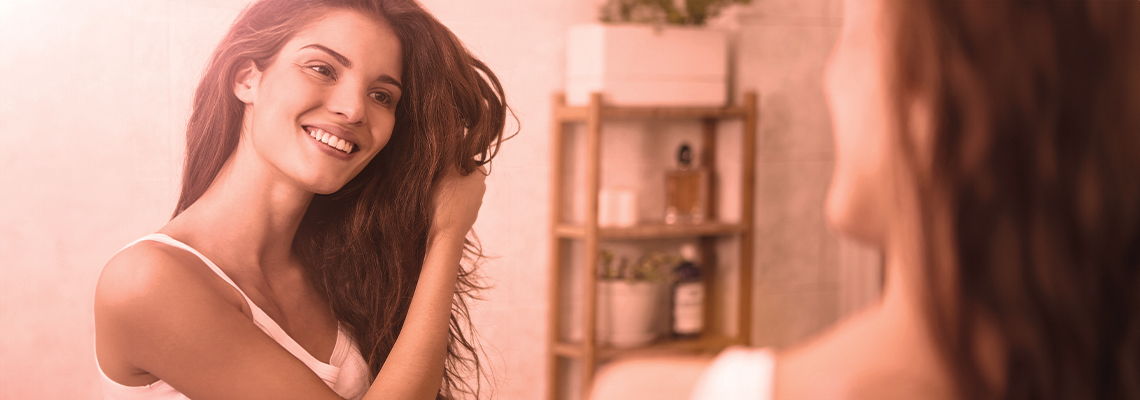 Smiling woman brushing her hair in front of a mirror.
