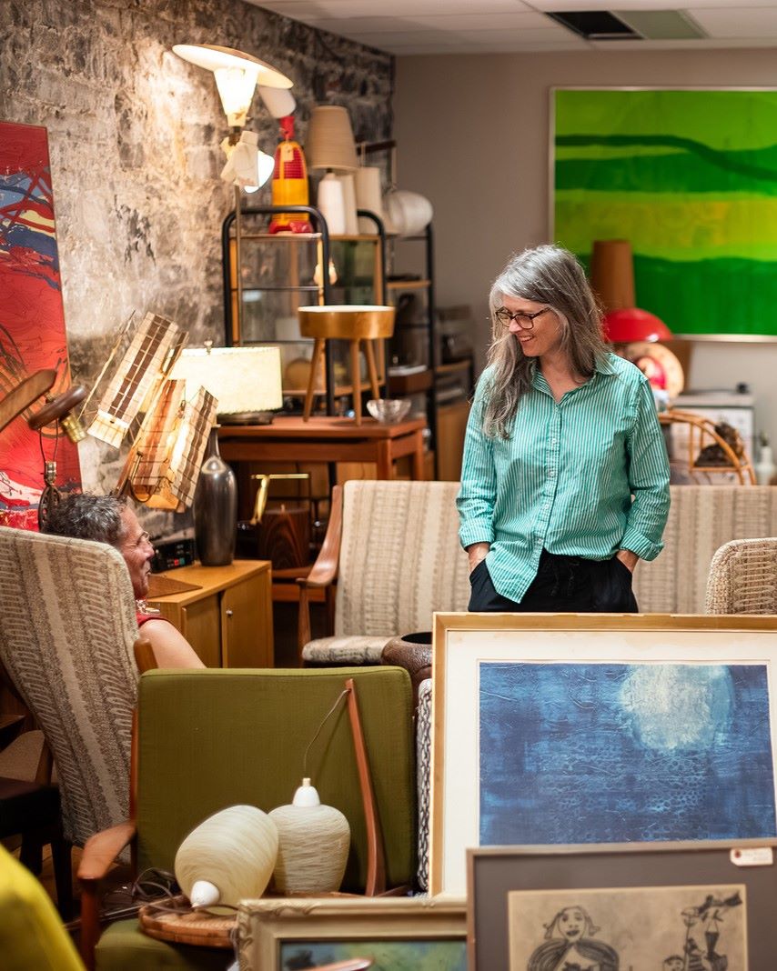 Person in a green shirt standing among vintage furniture and art.