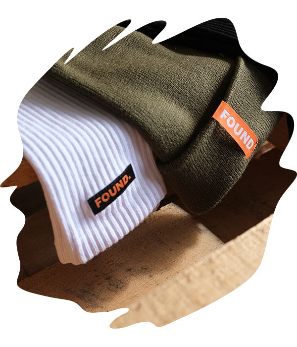 Stack of ribbed socks and beanies beanies in olive and white featuring an orange 