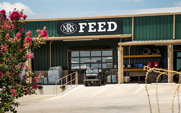 Storefront of a feed store with equipment and flowers in the foreground.