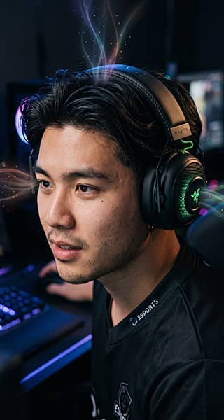 Person wearing gaming headphones, focused on a computer screen, colorful lighting effects.