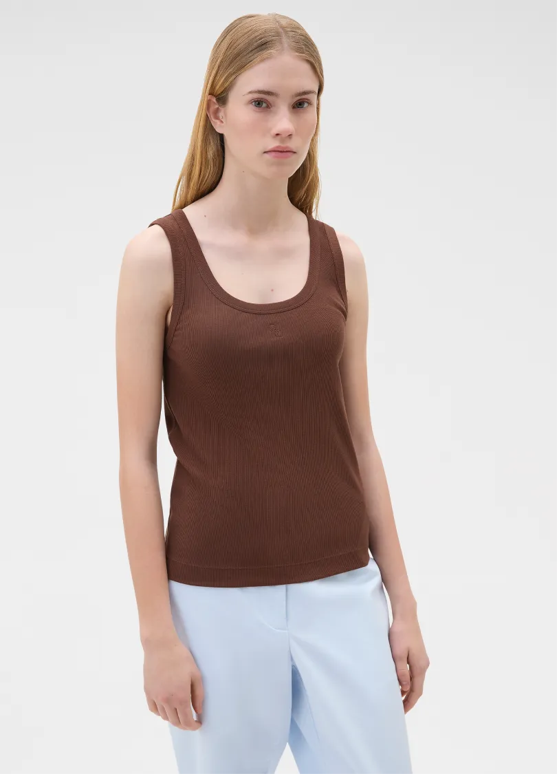 A young woman wearing a brown tank top and light blue pants.