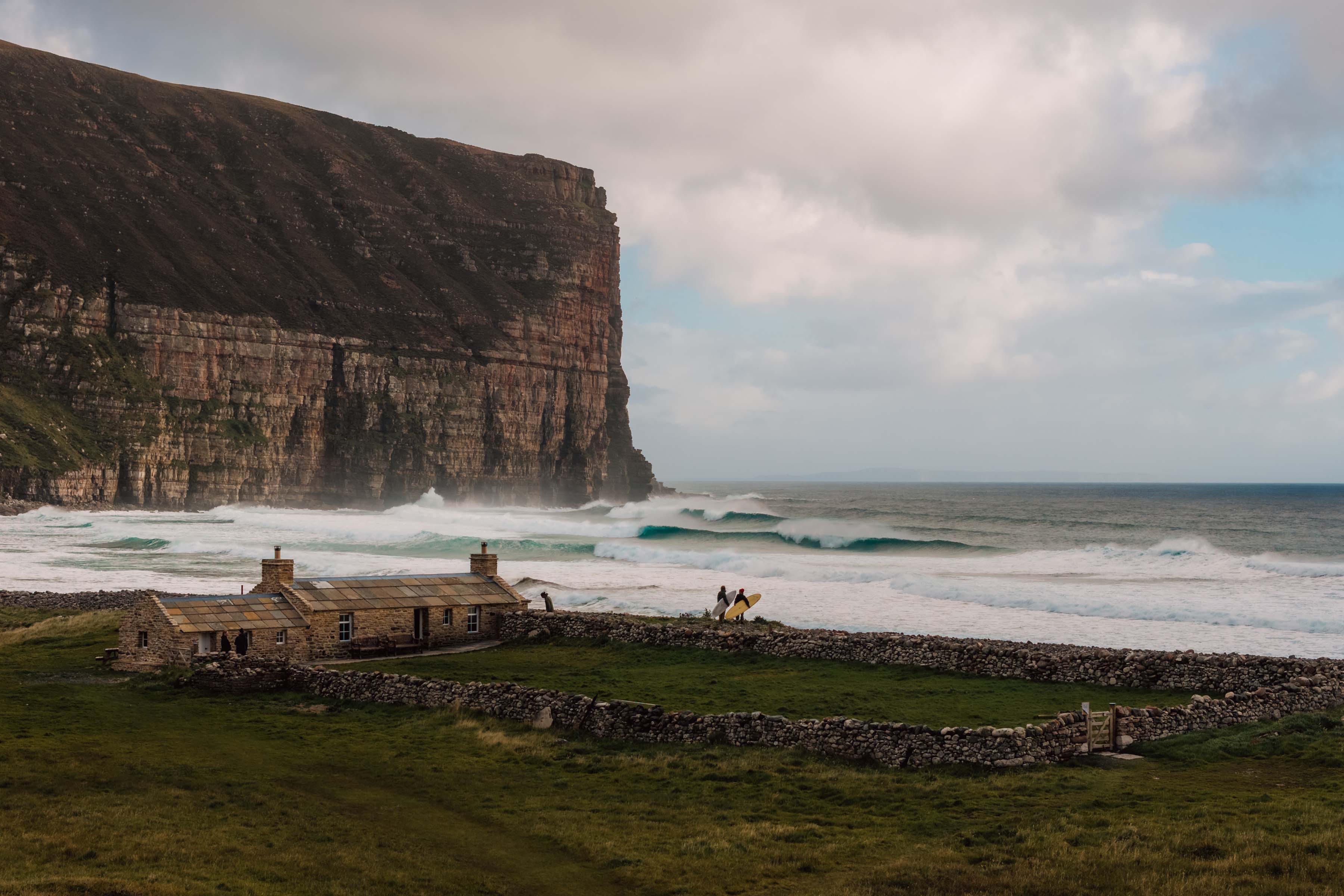Coastal landscape with cliffs, waves, and ruins on the shore.