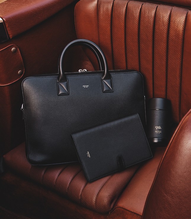 A black leather bag and a tablet on a brown leather seat.