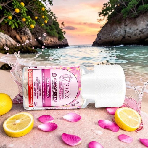 Bottle of skincare product on sandy beach with flowers and lemons.