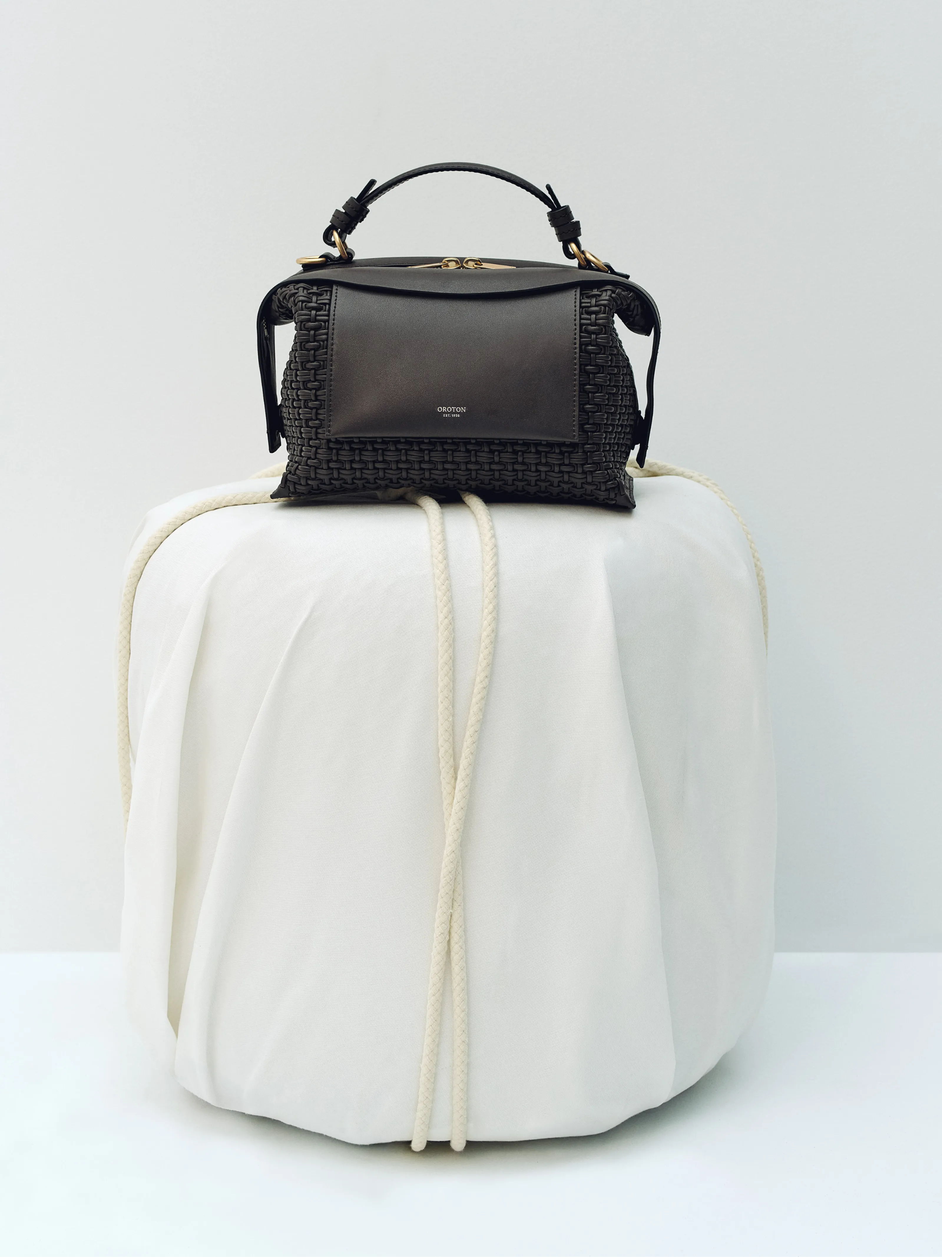 A stylish black handbag on a white, draped pedestal.