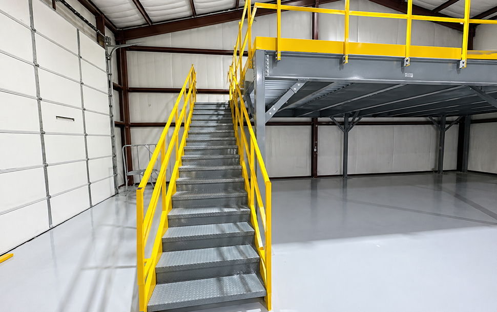 Interior of a warehouse featuring a staircase and elevated platform with yellow railings.