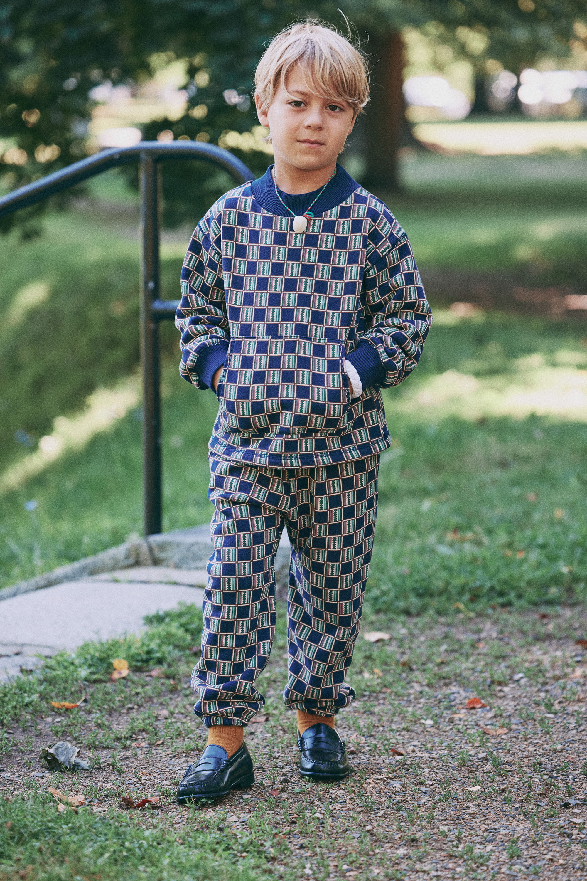 Child in patterned outfit standing outdoors with hands in pockets.