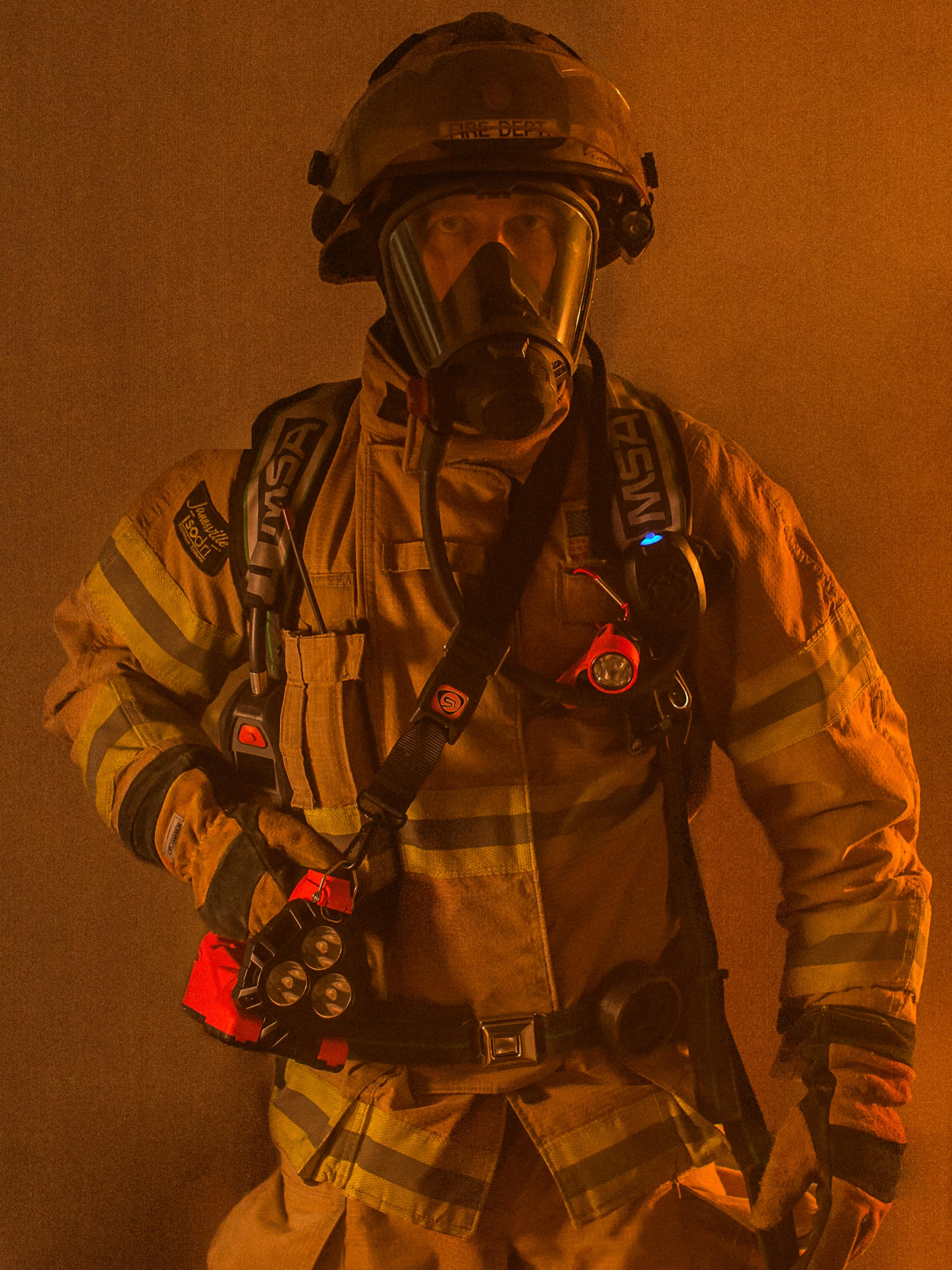 Firefighter in protective gear standing in smoky environment.