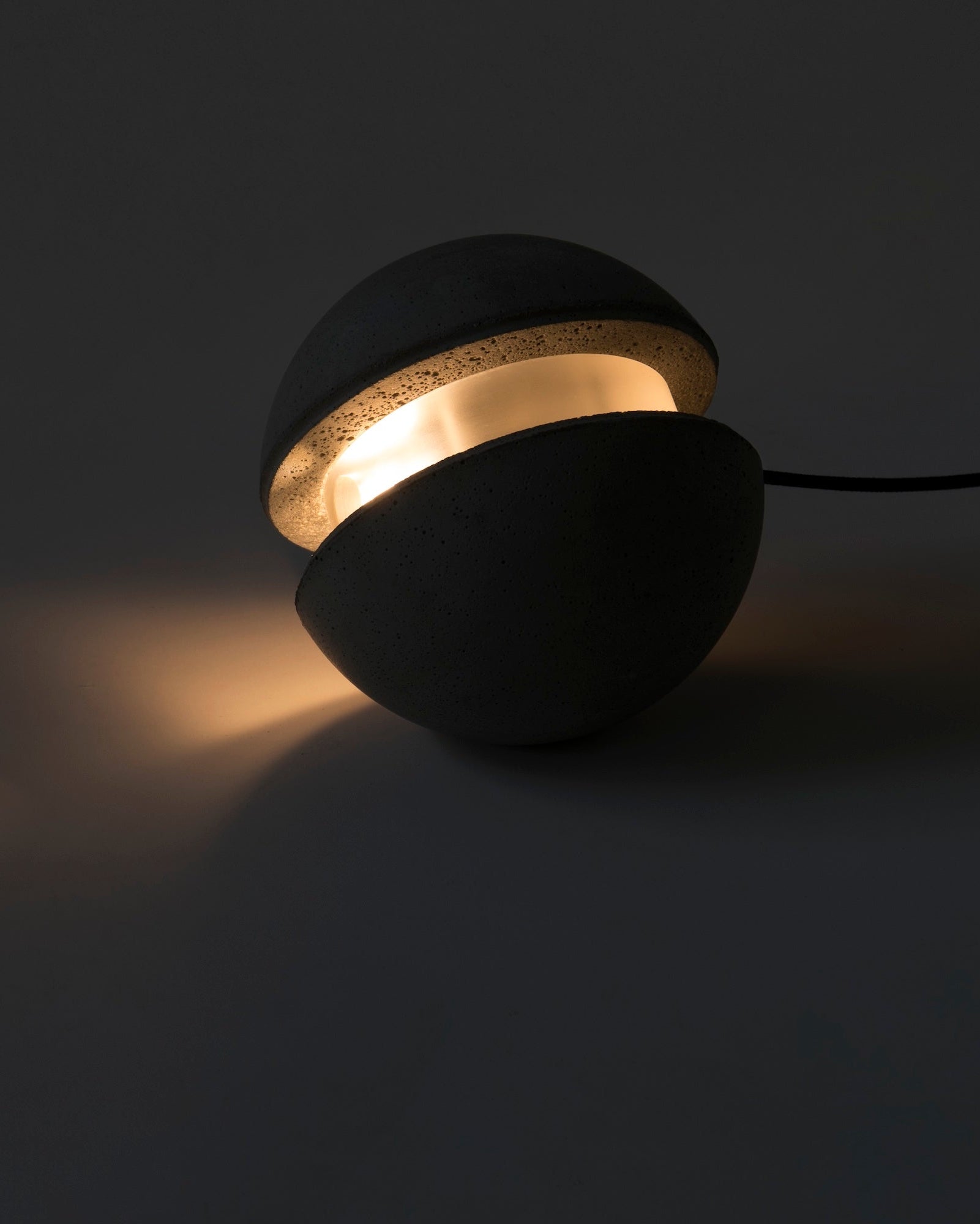 Dark concrete pendant with a glowing interior on a dark background