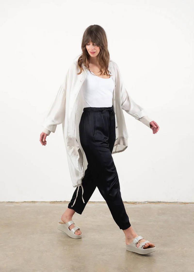A model wearing an off white, floaty unzipped jacket with a white top, black trousers an off white chunky slides