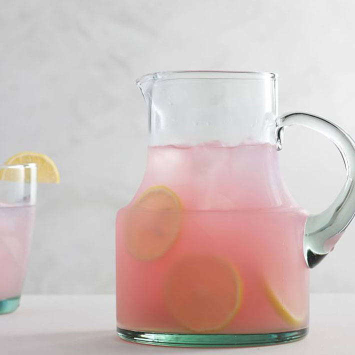 A glass pitcher with pink drink inside and lemons. 