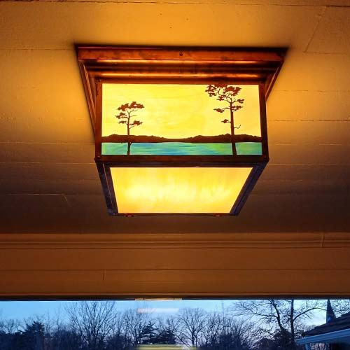 A ceiling square light with decorative tree artwork and a raw copper finish. It's illuminated.