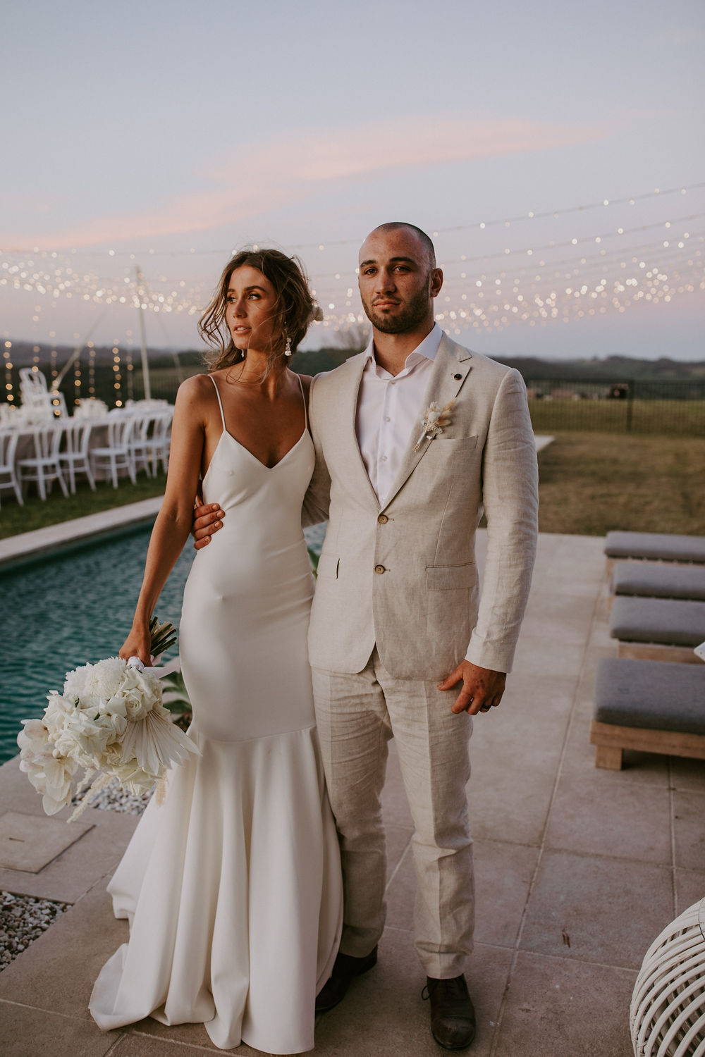 La novia con un vestido largo de seda con su novio al lado de la piscina