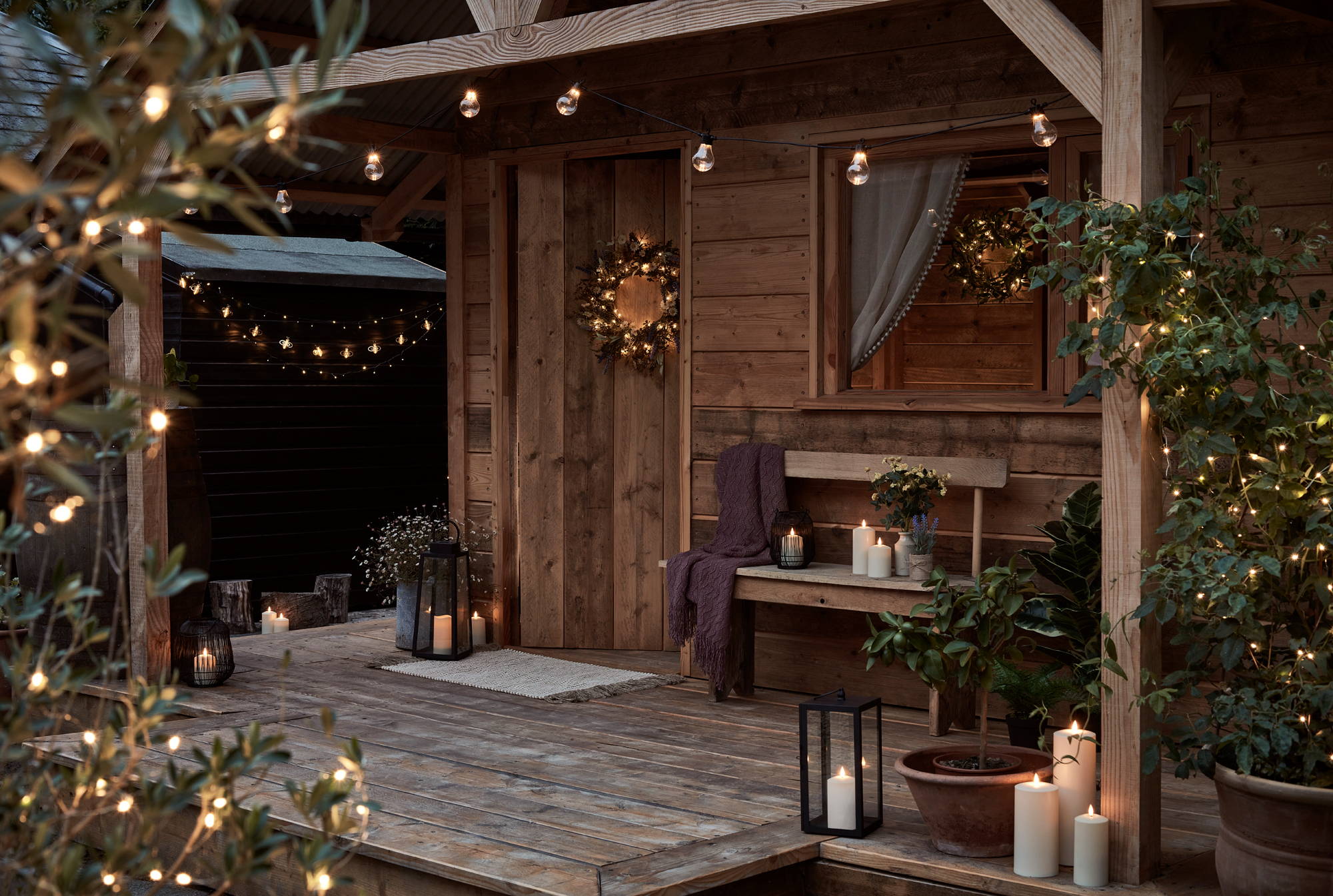 An outdoor summer house decorated with wreaths, lanterns, candles, fairy lights and festoons.