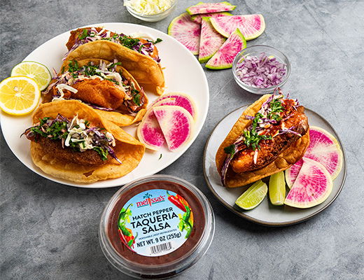 Tacos with salsa, radishes, and lime on a gray background.