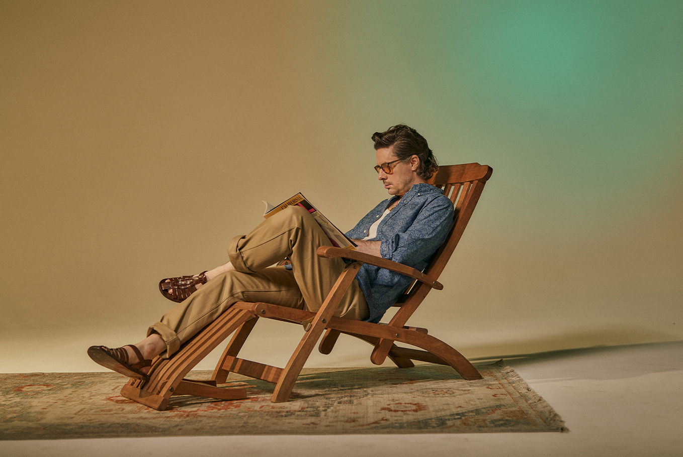 Person sitting in a chair, reading, with a neutral background.