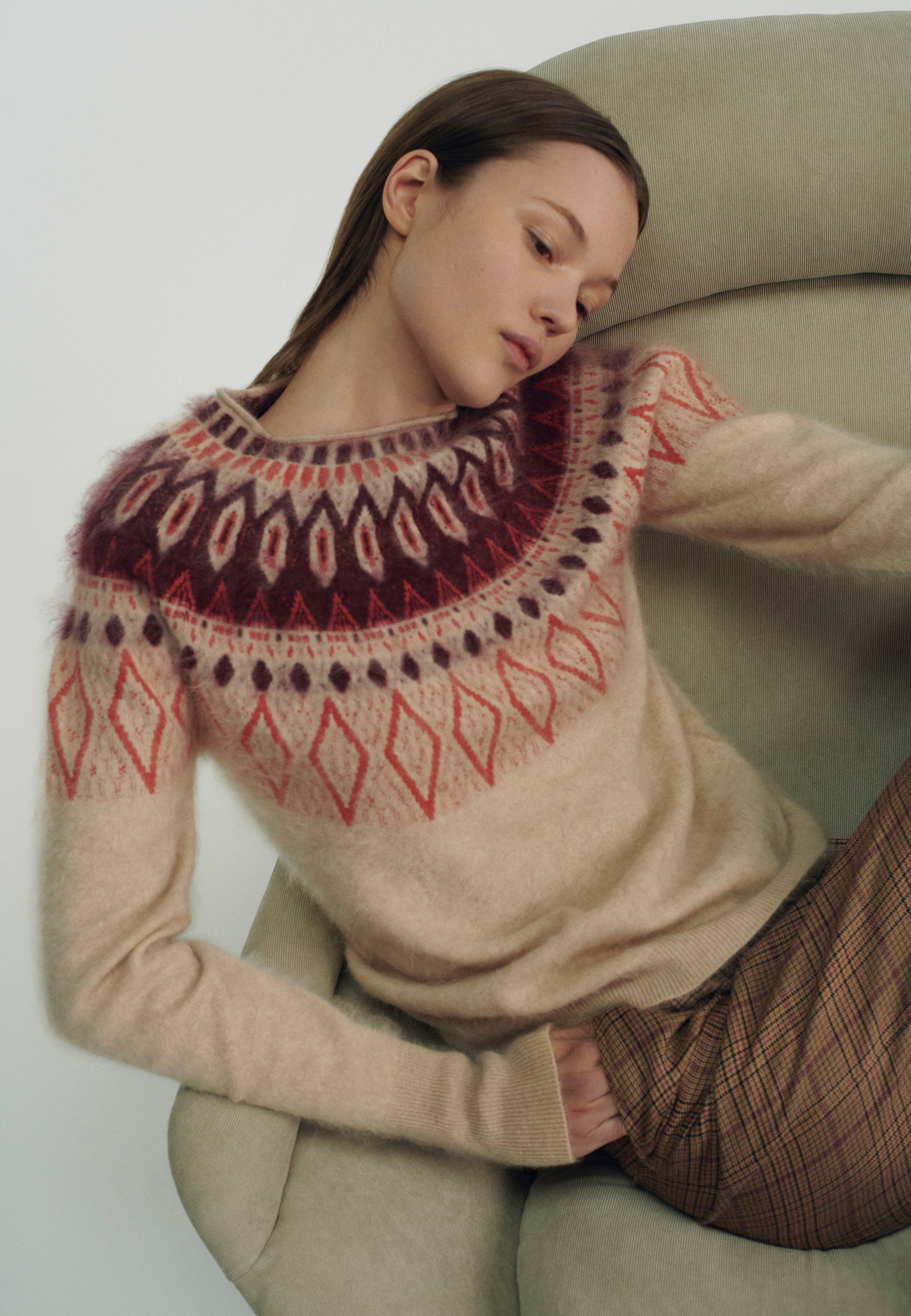 Woman in a patterned sweater sitting on a chair, striking a pose.