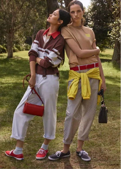 Two models in casual outfits posing in a grassy outdoor setting.