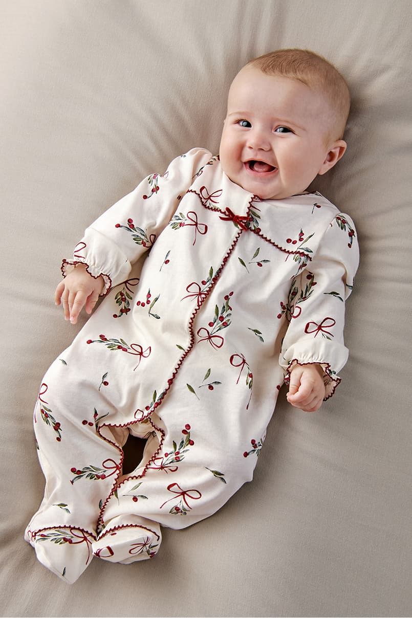 Baby smiling while wearing a floral-patterned onesie on a soft surface.