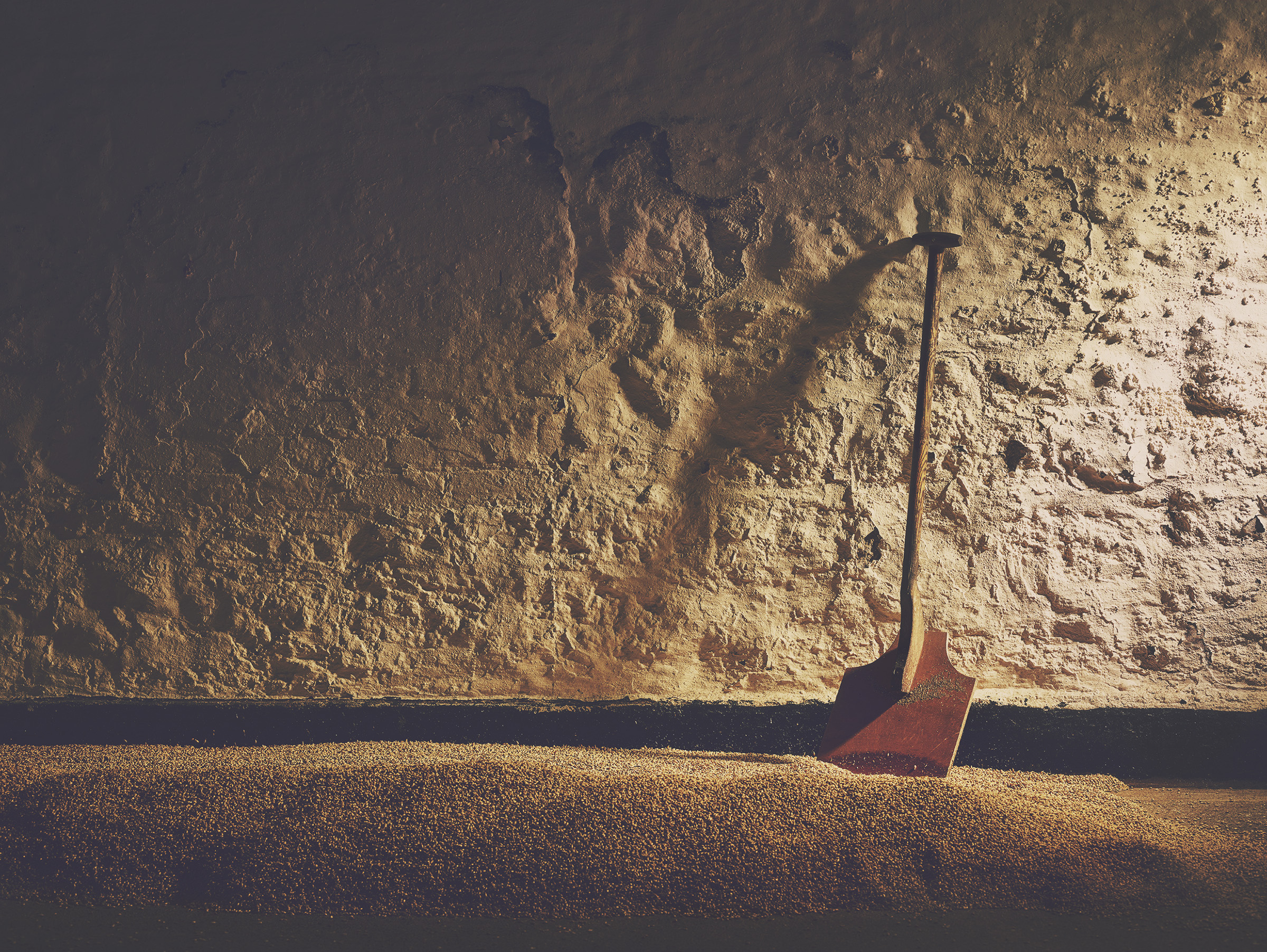 A wooden shovel leaning against a textured stone wall in dim light.