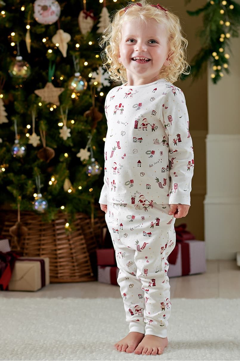 Child in festive pajamas smiling near a Christmas tree.