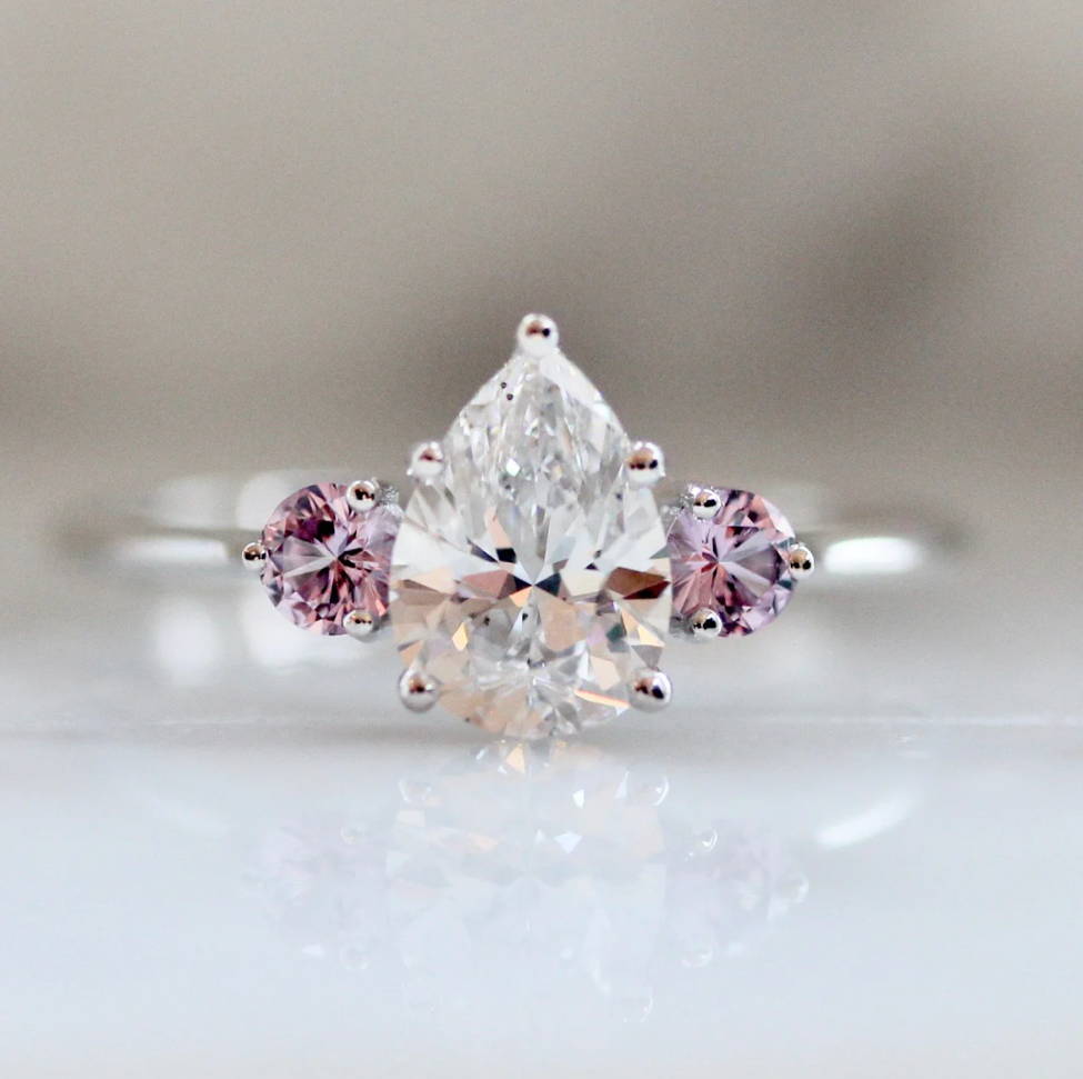 Pear shaped engagement ring with pink sapphire side stones