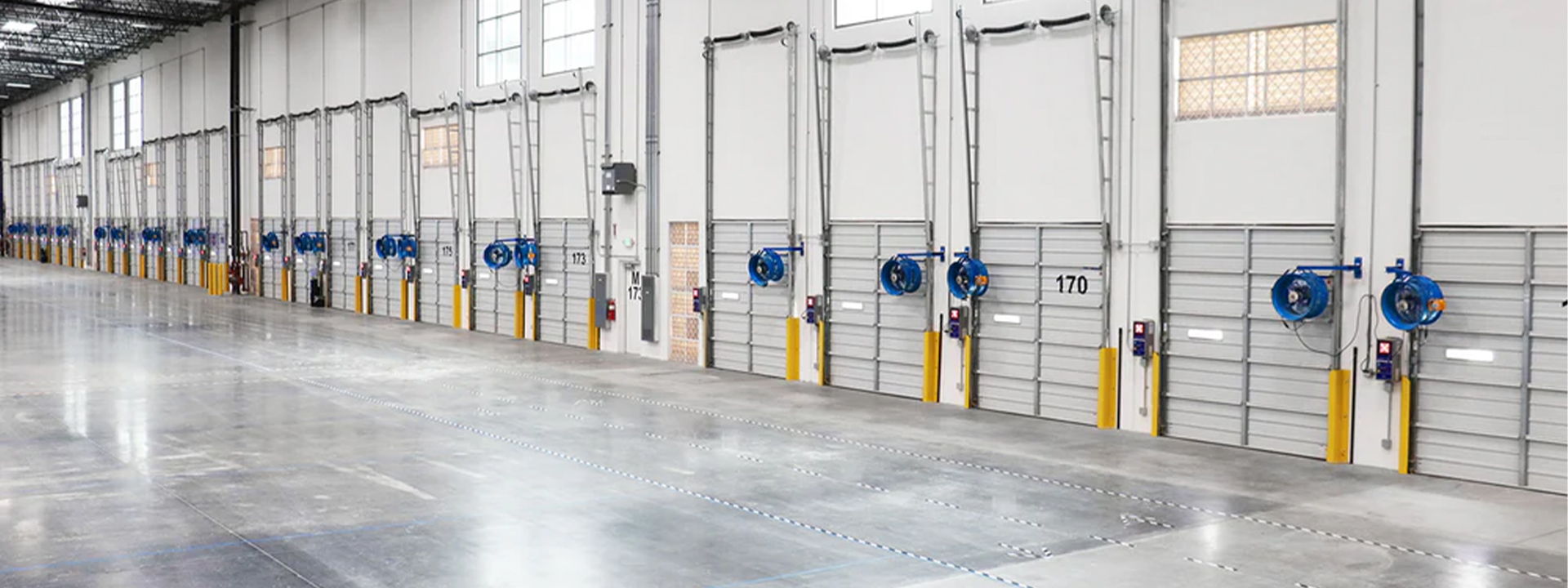 Interior of a large industrial building with multiple doors and concrete flooring.