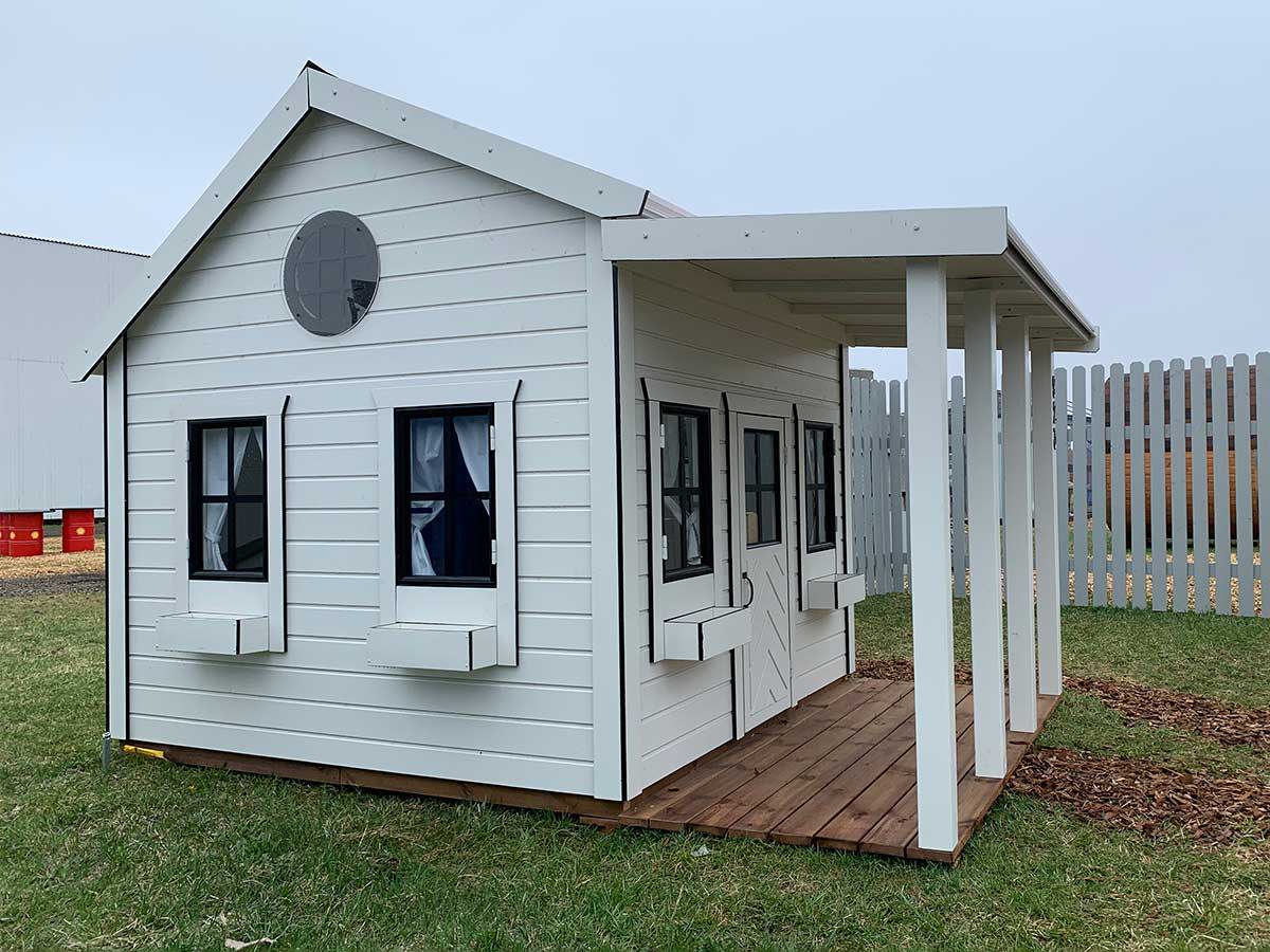 Custom Playhouse in white color with black trims  and  covered  porch on grass by WholeWoodPlayhouses
