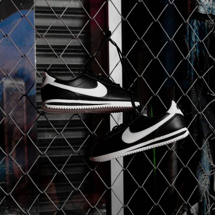 nike black and white cortez hanging on chain link fence