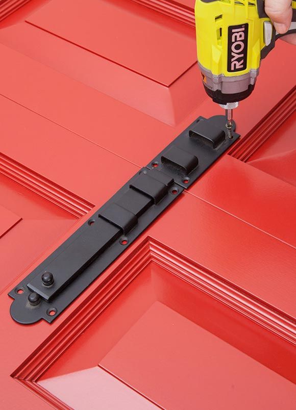 A person using a drill to install a black latch on a red door.
