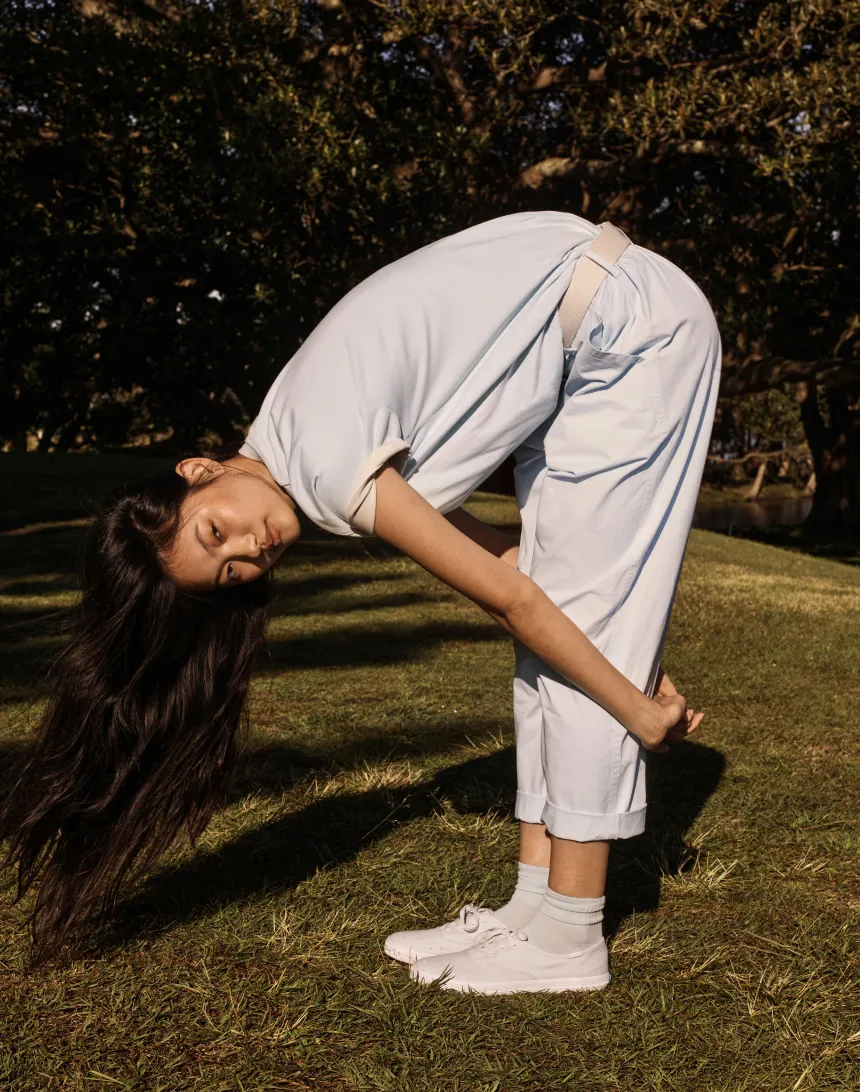 Person in casual clothing bent forward in a grassy outdoor setting.