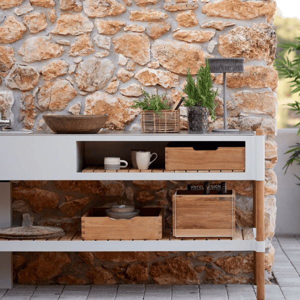 Outdoor console table with open storage, wood trays, and planters against a natural stone wall for organized patio entertaining