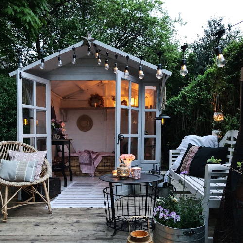Garden shed with festoons and a cosy seating area with trees in the background.