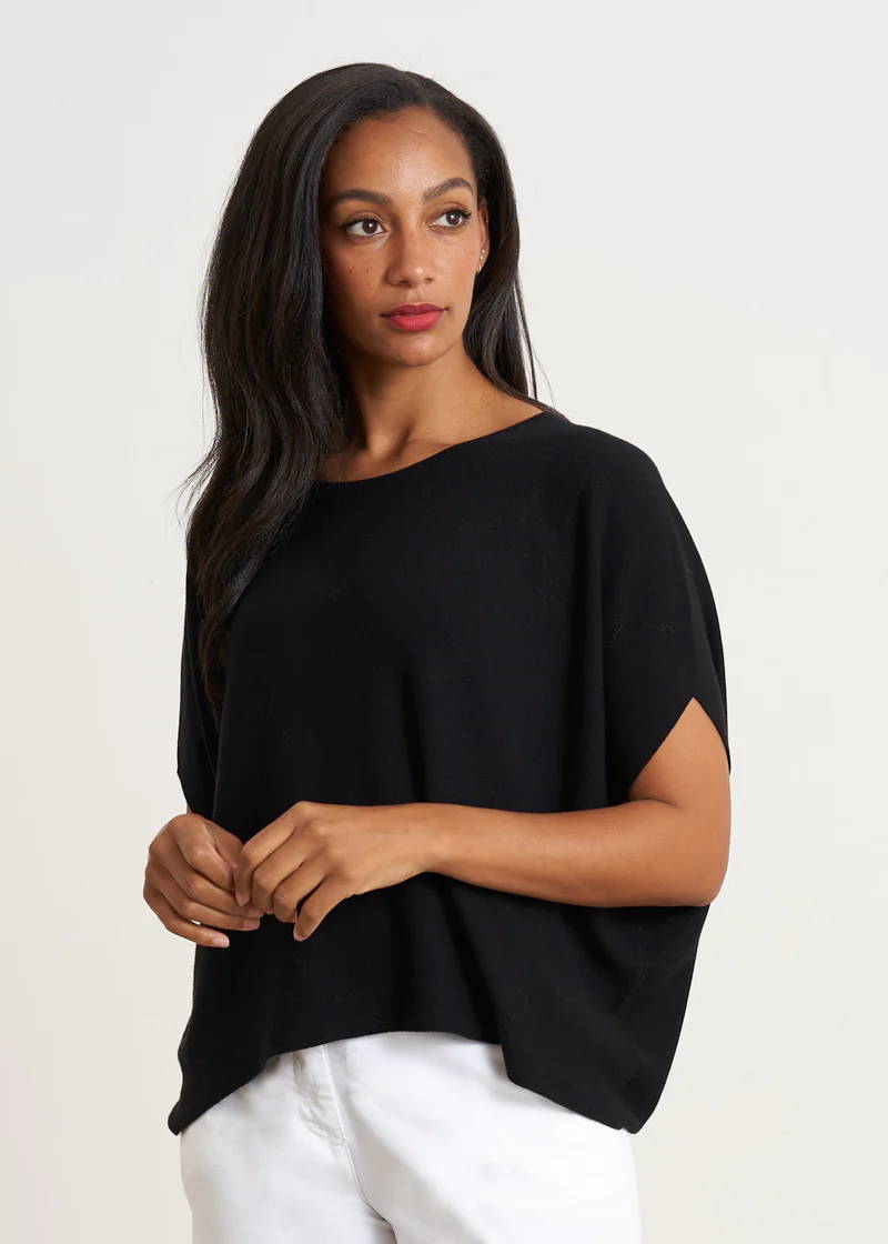 A model wearing a black, boxy, sleeveless sweater over white trousers