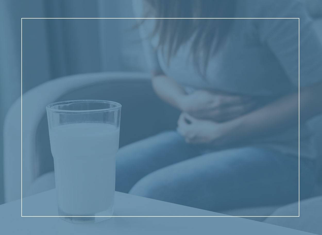 Femme aux cheveux longs se tenant le ventre après avoir bu un verre de lait. Les symptômes de l’APLV peuvent apparaître presque immédiatement