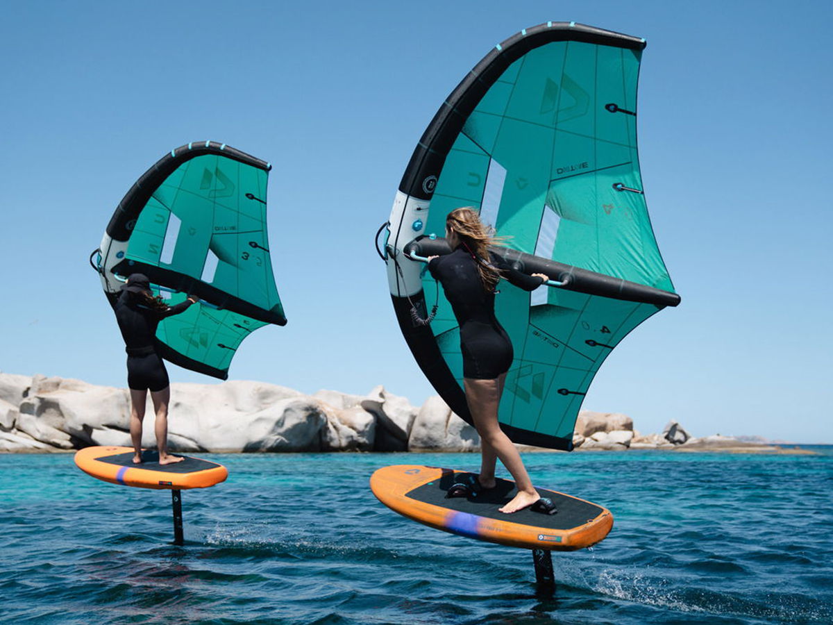 Two people foiling on water with colorful sails under a clear blue sky.